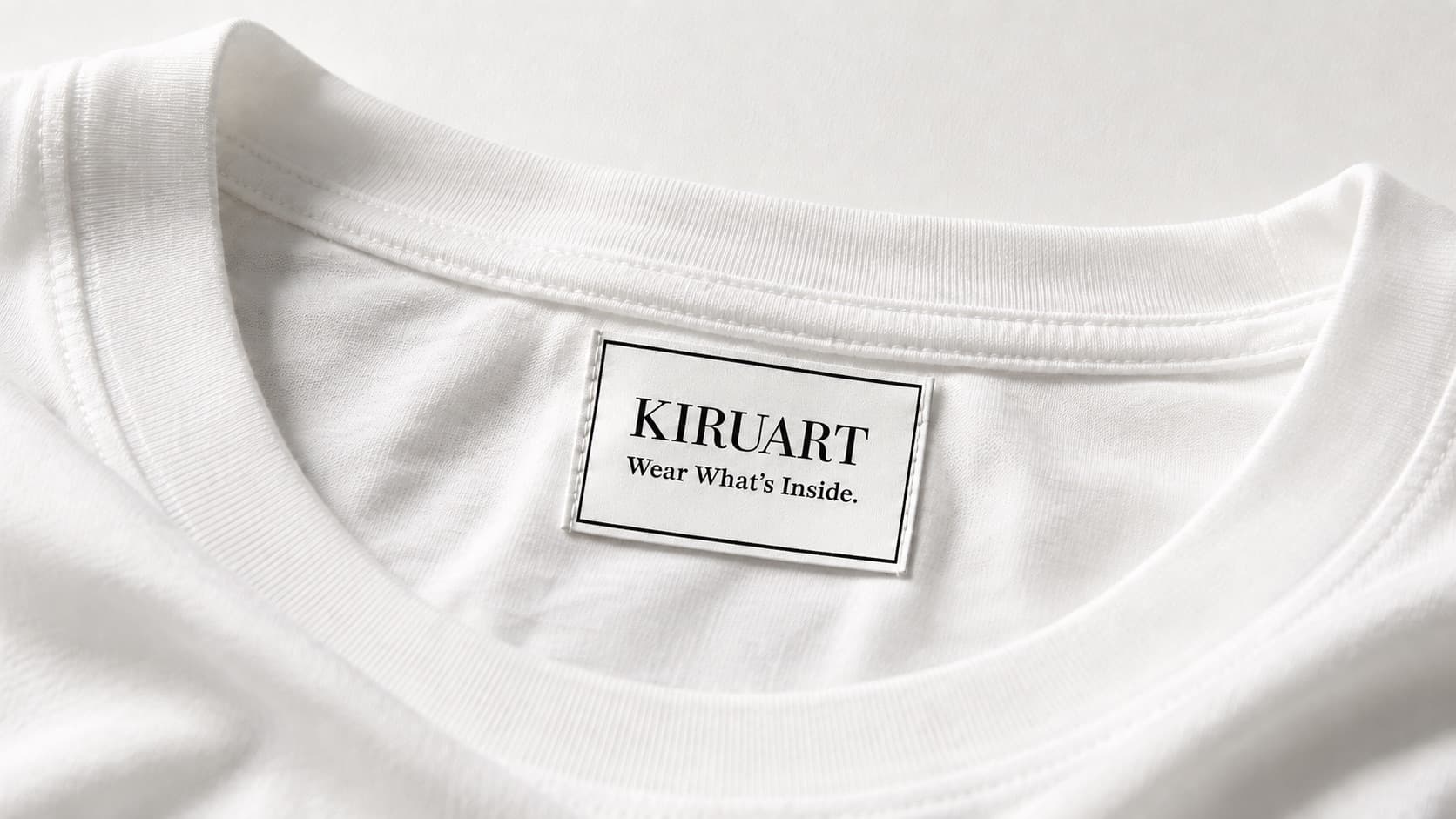 KIRUART のブランドタグを縫い付けた白いTシャツの襟元